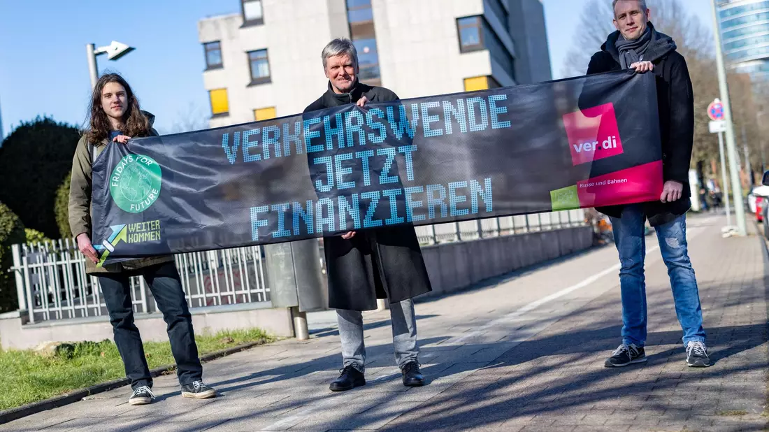 Emil Görtzen (l-r), Fridays for Future, Jürgen Schirmer, Gewerkschaft Verdi, und Patrick Steinbach, Verkehrsbetrieb BoGeStra, stehen mit einem Banner zum gemeinsamen Aktionstag vor der Verdi-Zentrale in Bochum. - Bild: Christoph Reichwein/dpa