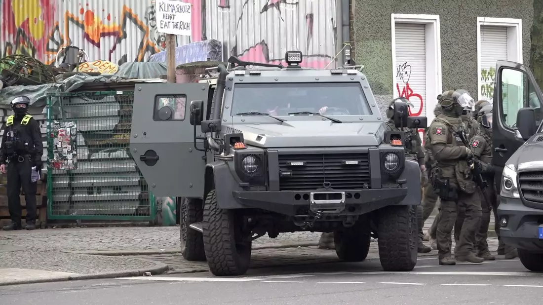 Polizisten an einem gepanzerten Fahrzeug. - Bild: Paul Zinken/dpa