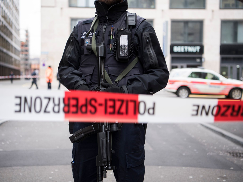 Ein schwer bewaffneter Polizist hinter einem Absperrband in der Züricher Innenstadt (Symbolbild). - Foto: Ennio Leanza/KEYSTONE/dpa