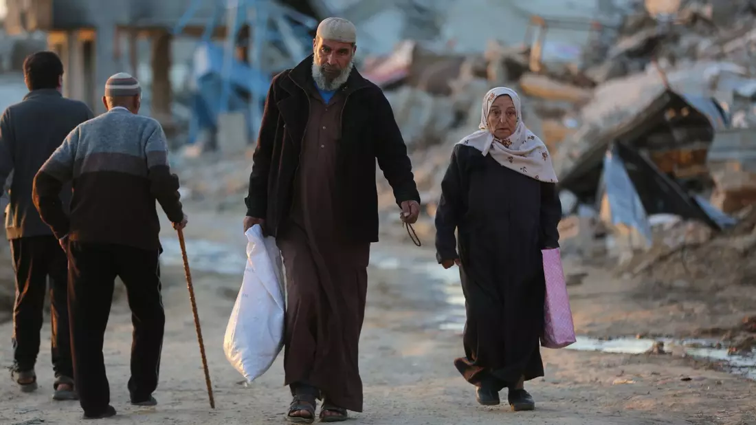 Menschen gehen an zerstörten Gebäuden im Flüchtlingslager Al-Maghazi im Zentrum des Gazastreifens vorbei. Das Bangen um eine Feuerpause vor Ramadan geht weiter. - Bild: -/XinHua/dpa