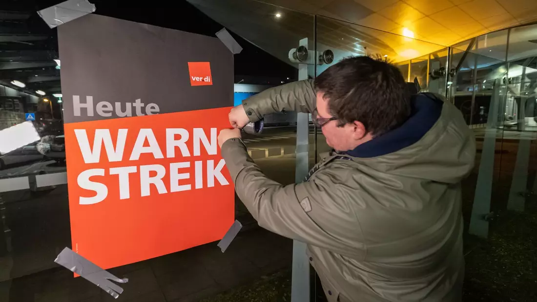 Streikende hängen Plakate mit der Aufschrift «Warnstreik» bei der Lufthansa Technik auf. Mit erneuten Warnstreiks gleich mehrerer Berufsgruppen legt die Gewerkschaft Verdi am Donnerstag und Freitag wichtige Teile des deutschen Luftverkehrs lahm. - Bild: Bodo Marks/dpa