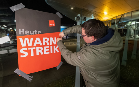 Streikende hängen Plakate mit der Aufschrift «Warnstreik» bei der Lufthansa Technik auf. Mit erneuten Warnstreiks gleich mehrerer Berufsgruppen legt die Gewerkschaft Verdi am Donnerstag und Freitag wichtige Teile des deutschen Luftverkehrs lahm. - Foto: Bodo Marks/dpa