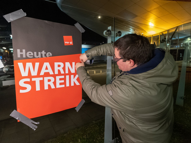 Streikende hängen Plakate mit der Aufschrift «Warnstreik» bei der Lufthansa Technik auf. Mit erneuten Warnstreiks gleich mehrerer Berufsgruppen legt die Gewerkschaft Verdi am Donnerstag und Freitag wichtige Teile des deutschen Luftverkehrs lahm. - Foto: Bodo Marks/dpa