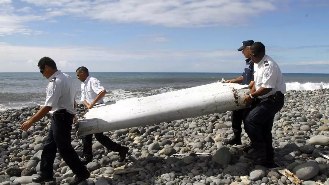 Techniker tragen ein Wrackteil, die Flügelklappe eines Flugzeugs, über einen Strand bei Saint-André,  Réunion. - Bild: Raymond Wae Tion/MAXPPP/QUOTIDIEN DE LA REUNION/dpa