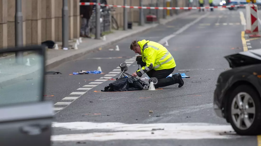 Ein Polizist kniet an der Unfallstelle neben dem zerstörten Kinderwagen. - Bild: Christophe Gateau/dpa