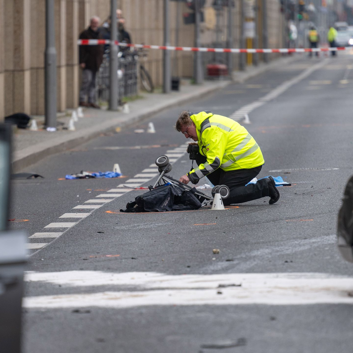 Ein Polizist kniet an der Unfallstelle neben dem zerstörten Kinderwagen. - Foto: Christophe Gateau/dpa