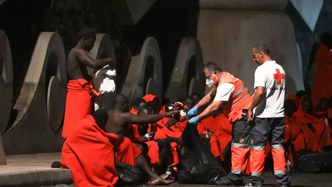 Mitarbeiter des Roten Kreuzes verteilen im November Wasser an Migranten an einer Anlegestelle im Hafen von La Restinga auf der kanarischen Insel El Hierro. - Bild: Humberto Bilbao/AP/dpa