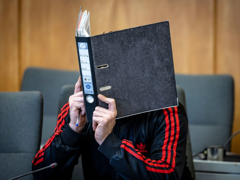 Der Angeklagte verbirgt im Landgericht sein Gesicht hinter einem Aktenordner. - Foto: Christoph Reichwein/dpa