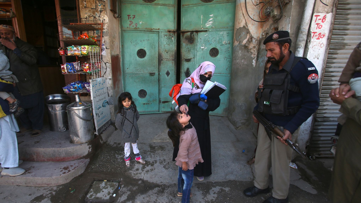 Ein Polizist in Pakistan steht Wache, während einem Kind ein Polio-Impfstoff verabreicht wird. - Foto: Muhammad Sajjad/AP/dpa