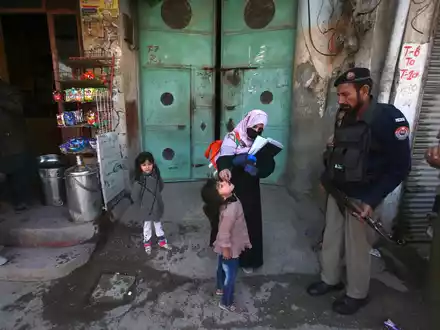 Ein Polizist in Pakistan steht Wache, während einem Kind ein Polio-Impfstoff verabreicht wird. - Foto: Muhammad Sajjad/AP/dpa