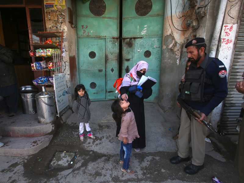 Ein Polizist in Pakistan steht Wache, während einem Kind ein Polio-Impfstoff verabreicht wird. - Foto: Muhammad Sajjad/AP/dpa