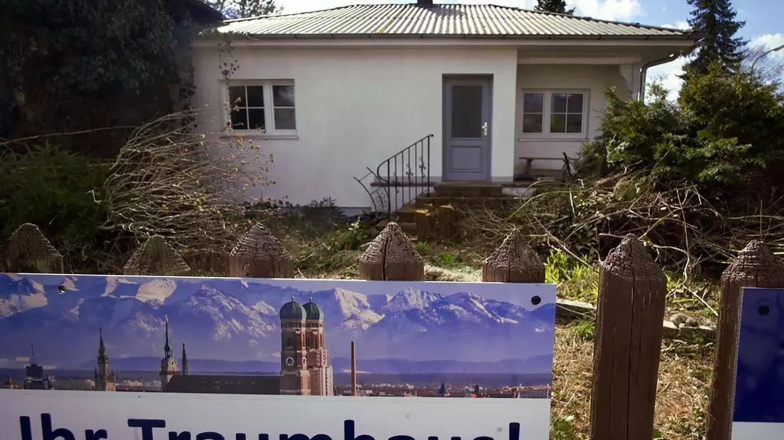 Ein zum Abriss bestimmtes Münchner Einfamilienhaus mitsamt dem Werbeplakat einer Immobiliengesellschaft. - Bild: Carsten Hoefer/dpa