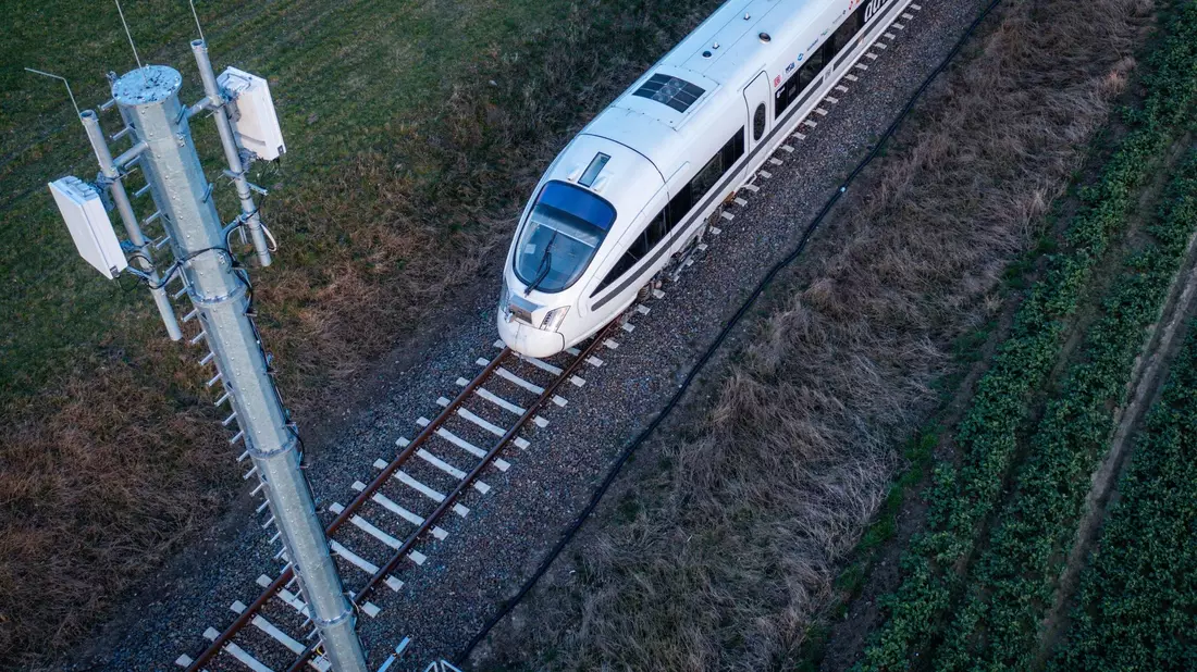 Ein Testzug der Deutschen Bahn fährt an einer der Antennenmasten für das 5G-Bahnprojekt vorbei. - Bild: Jens Büttner/dpa