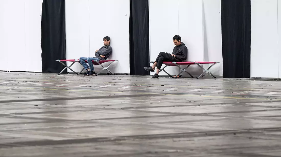 Geflüchtete sitzen auf Feldbetten in einer Massenunterkunft in Frankfurt: Viele Geflüchtete wünschen sich mehr Hilfe in Asyl- und Flüchtlingsfragen. - Bild: Boris Roessler/dpa