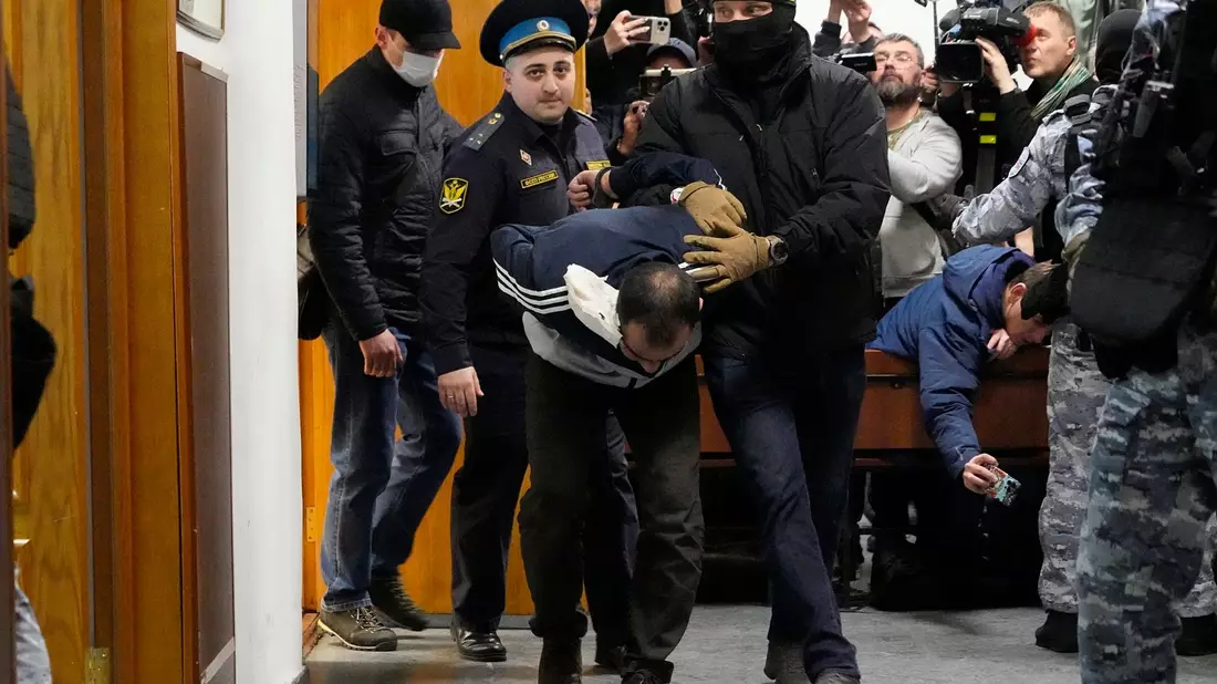 Ein Tatverdächtiger wird von Polizisten und FSB-Beamten im Basmanny-Bezirksgericht eskortiert. - Bild: Alexander Zemlianichenko/AP