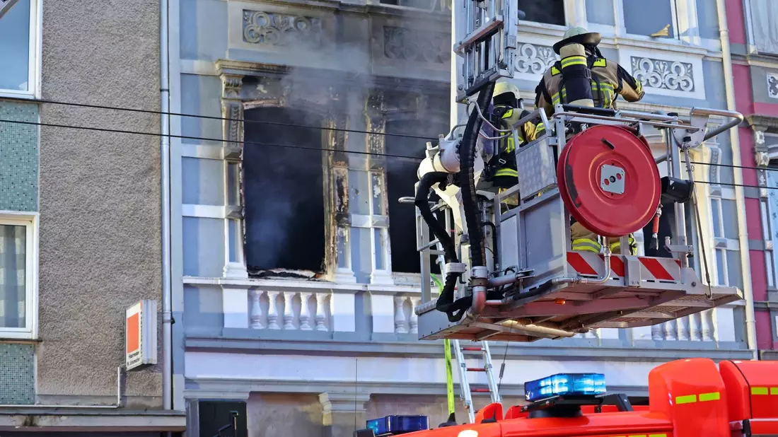 Feuerwehrmänner stehen vor dem Mehrfamilienhaus, in dem es gebrannt hat. - Bild: Gianni Gattus/Blaulicht Solingen/dpa