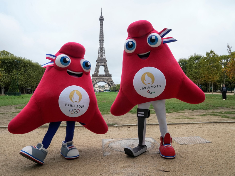 Die Maskottchen der Olympischen (l) und Paralympischen Spiele in Paris stehen vor dem Eiffelturm. - Foto: Michel Euler/AP/dpa