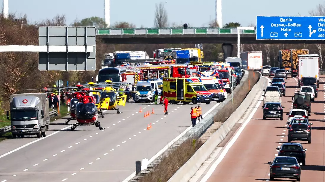 Ein Feuerwehrmann untersucht den Reisebus hinter mobilen Sichtschutzwänden. - Bild: Jan Woitas/dpa