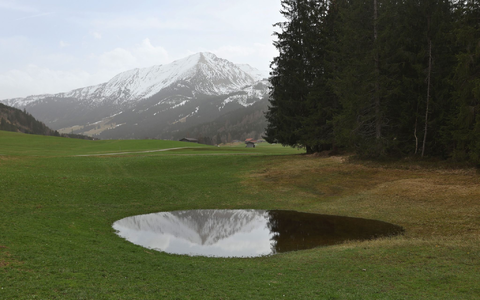 Die im Dunst liegenden Alpen spiegeln sich in einem Weiher. Der Saharastaub-Höhepunkt ist überschritten. - Foto: Karl-Josef Hildenbrand/dpa