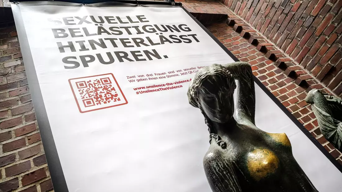 Plakat mit der Aufschrift «Sexuelle Belästigung hinterlässt Spuren» hinter der Bronzeskulptur «Jugend» von Bernhard Hoetger in Bremen. - Bild: Sina Schuldt/dpa