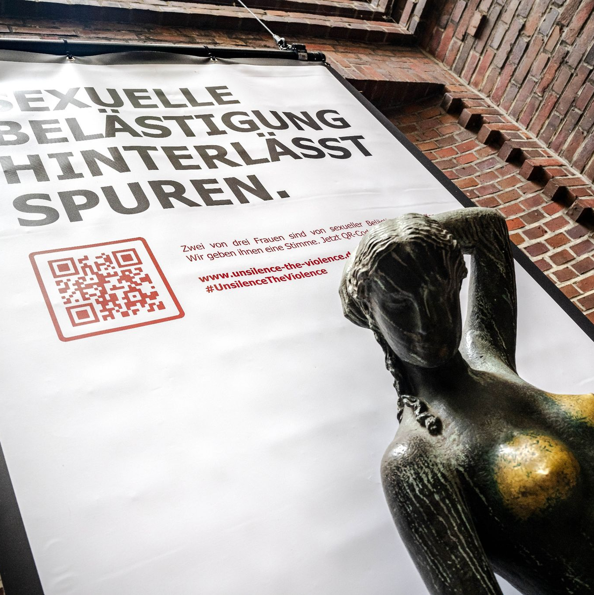 Plakat mit der Aufschrift «Sexuelle Belästigung hinterlässt Spuren» hinter der Bronzeskulptur «Jugend» von Bernhard Hoetger in Bremen. - Foto: Sina Schuldt/dpa