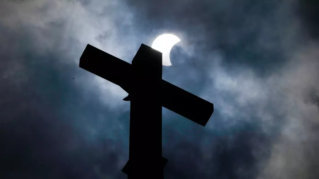 Wolken lösen sich auf und geben über dem Kreuz eines Kirchturms in Manor (Texas) den Blick auf die beginnende Sonnenfinsternis frei. - Bild: Charles Rex Arbogast/AP