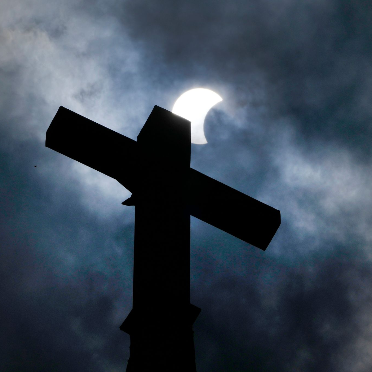 Wolken lösen sich auf und geben über dem Kreuz eines Kirchturms in Manor (Texas) den Blick auf die beginnende Sonnenfinsternis frei. - Foto: Charles Rex Arbogast/AP