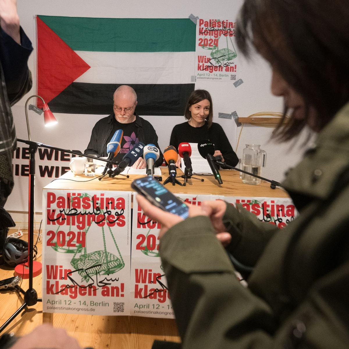 Teilnehmer sitzen vor Beginn des Palästina-Kongress 2024 im Veranstaltungsraum vor einem Plakat des Kongresses. - Foto: Sebastian Christoph Gollnow/dpa