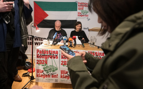 Teilnehmer sitzen vor Beginn des Palästina-Kongress 2024 im Veranstaltungsraum vor einem Plakat des Kongresses. - Foto: Sebastian Christoph Gollnow/dpa