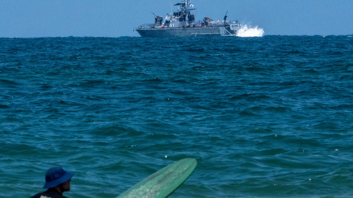 Ein Surfer wartet auf eine Welle, während ein israelisches Marineschiff im Mittelmeer vor der Küste von Hadera patrouilliert. - Foto: Ariel Schalit/AP