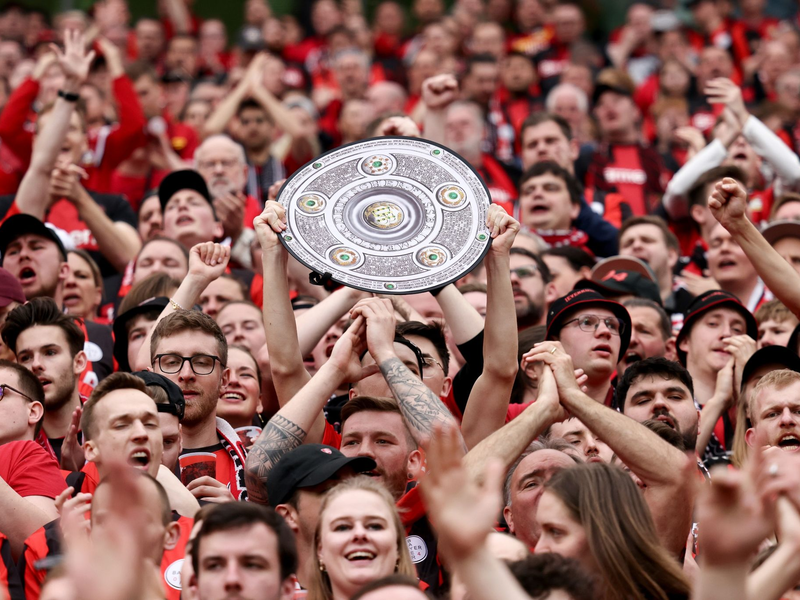Fußball: Ein Leverkusener Fan hält während des Spiels eine Nachbildung der Meisterschale in den Händen. Bayer Leverkusen gewinnt die Deutsche Meisterschaft. - Foto: Rolf Vennenbernd/dpa