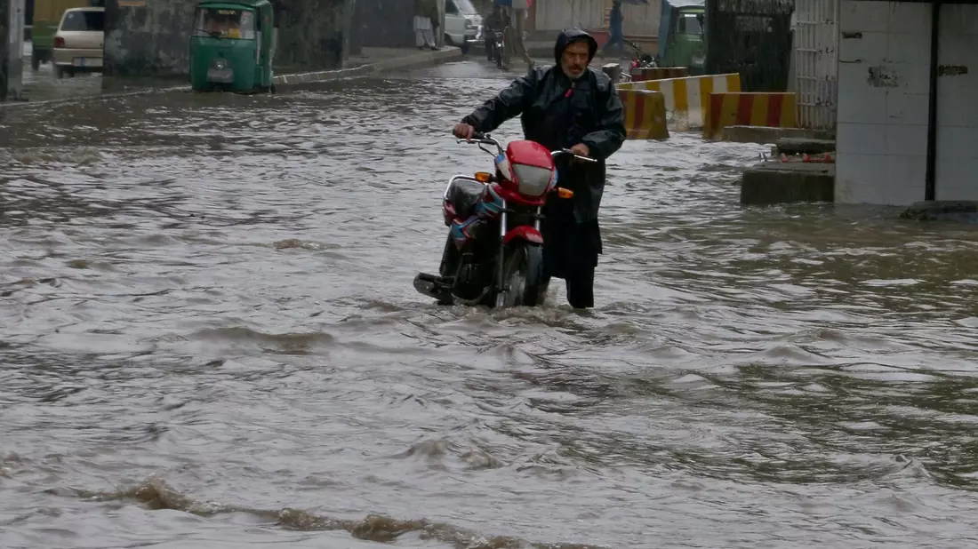 Ein Pakistaner watet nach starken Regenfällen mit seinem Motorrad durch eine überschwemmte Straße in Peschawar. - Bild: Muhammad Sajjad/AP/dpa