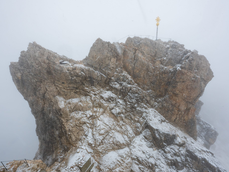 Nebelwolken umhüllen bei Schneetreiben auf der Zugspitze die Aussichtsplattform mit dem Gipfelkreuz (Archivbild). Aus 
mehreren Bergsteigergruppen wurden Notrufe abgesetzt, nachdem sie aufgrund von Witterung und Neuschnee auf etwa 2500 Metern Höhe nicht mehr weiterkamen. - Foto: Peter Kneffel/dpa