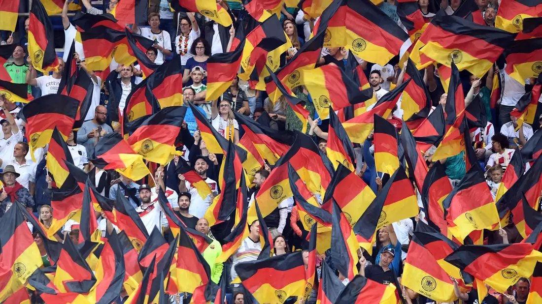 Fans schwenken Deutschlandfahnen auf der Tribüne. - Bild: Uli Deck/dpa