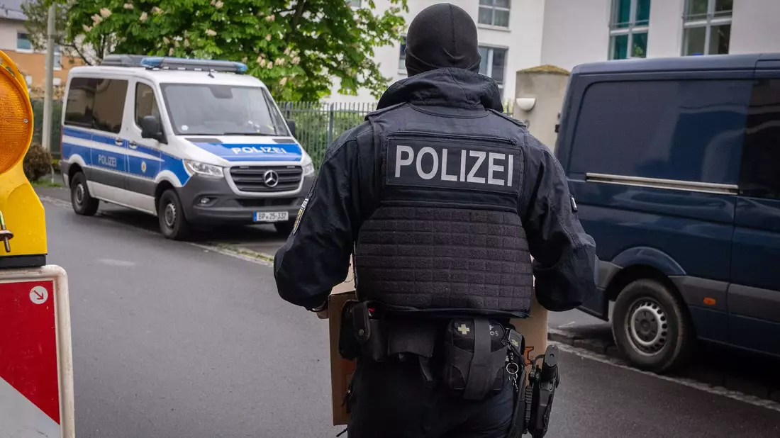 Ein Polizist trägt bei einem Einsatz in Bonn einen Karton mit beschlagnahmtem Material aus einem Gebäude. - Bild: Benjamin Westhoff/dpa