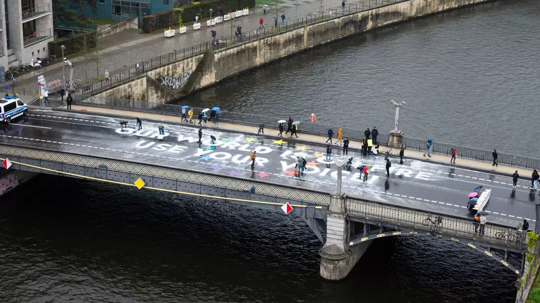 Klimaaktivisten der Bewegung Fridays for Future malen auf der Marschallbrücke in Berlin den Schriftzug «Our world is on fire - use your voice!». - Bild: Christophe Gateau/dpa