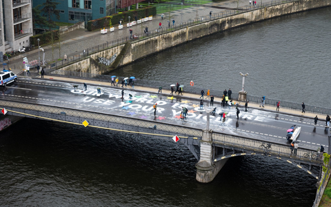 Klimaaktivisten der Bewegung Fridays for Future malen auf der Marschallbrücke in Berlin den Schriftzug «Our world is on fire - use your voice!». - Foto: Christophe Gateau/dpa
