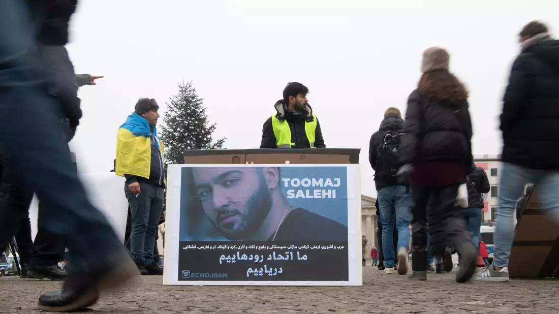 Protestaktion gegen Irans Staatsführung auf dem Pariser Platz in Berlin. Auf dem Plakat ist der Rapper Salehi zu sehen. - Bild: Paul Zinken/dpa
