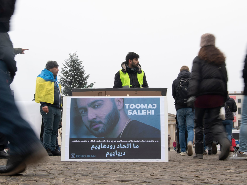 Protestaktion gegen Irans Staatsführung auf dem Pariser Platz in Berlin. Auf dem Plakat ist der Rapper Salehi zu sehen. - Foto: Paul Zinken/dpa