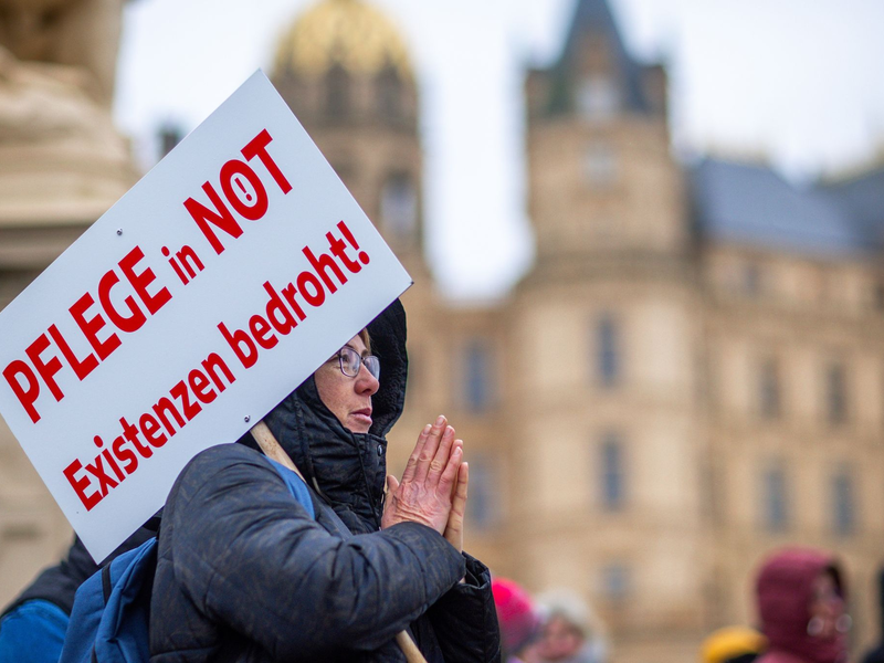 Bei einer Protestaktion vor dem Schweriner Landtag hält eine Teilnehmerin ein Schild mit der Aufschrift «Pflege in Not - Existenzen bedroht!». - Foto: Jens Büttner/dpa