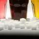 Drei Gläser gefüllt mit roter Limonade, Cola und einem Energy-Drink neben Zuckerwürfeln auf einem Tisch - Bild: Monika Skolimowska/dpa
