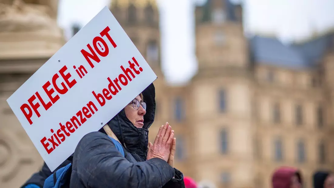 Bei einer Protestaktion vor dem Schweriner Landtag hält eine Teilnehmerin ein Schild mit der Aufschrift «Pflege in Not - Existenzen bedroht!». - Bild: Jens Büttner/dpa