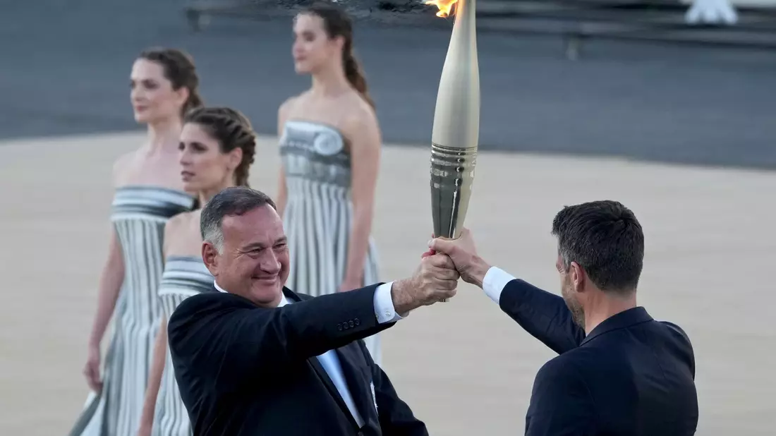 Der Präsident des französischen Organisationskomitees, Tony Estanguet (r), nahm die olympische Flamme in Athen entgegen. - Bild: Petros Giannakouris/AP/dpa