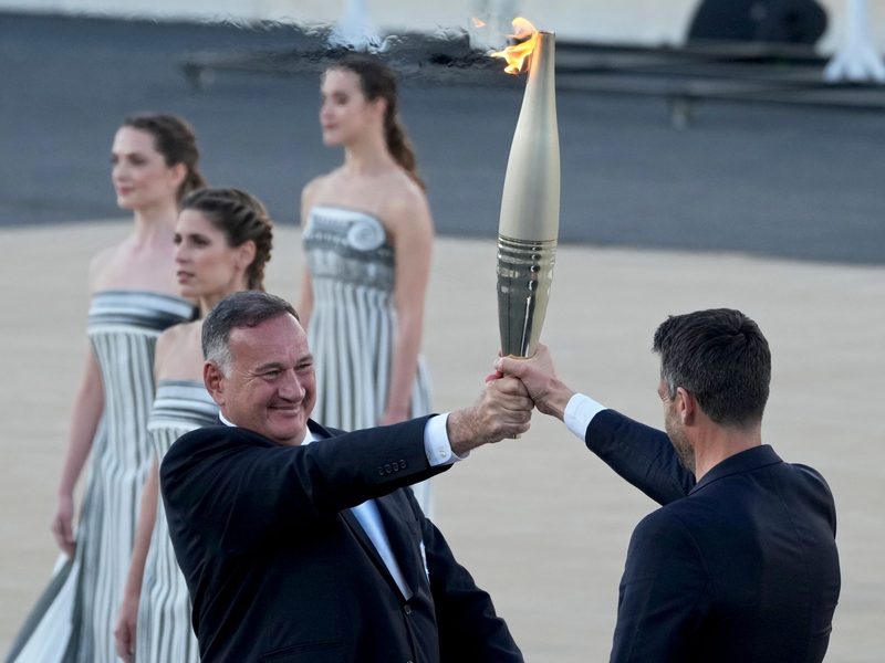 Der Präsident des französischen Organisationskomitees, Tony Estanguet (r), nahm die olympische Flamme in Athen entgegen. - Foto: Petros Giannakouris/AP/dpa