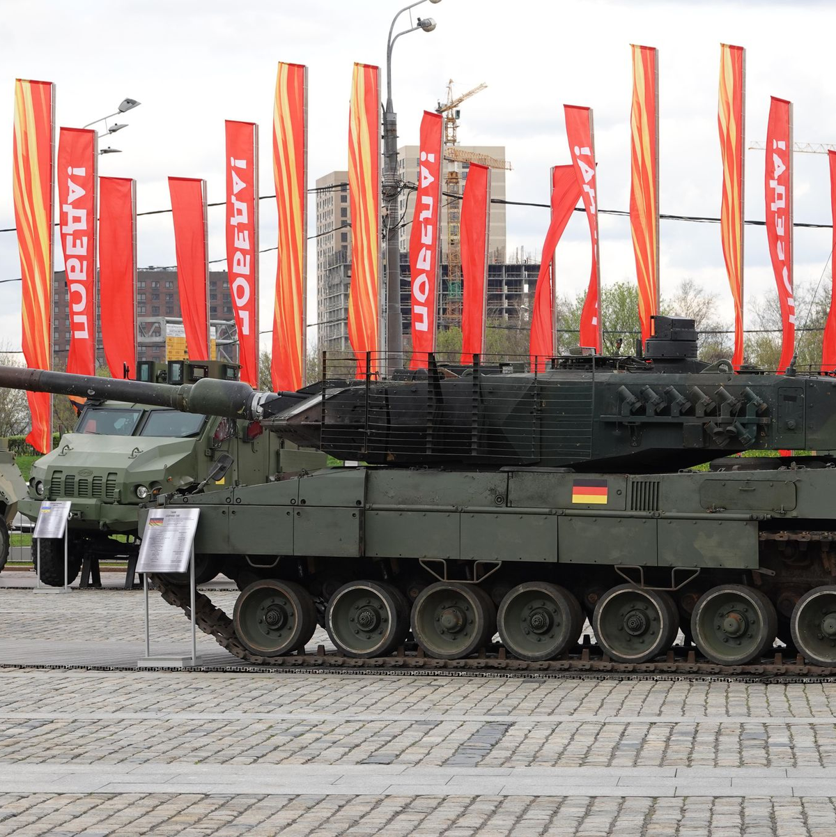Menschen besichtigen eine Schau zu Kriegstrophäen im Park Pobedy (Park des Sieges) in Moskau. Gezeigt wird Militärtechnik aus verschiedenen westlichen Ländern und der Ukraine. Im Hintergrund zu sehen sind rote Fahnen mit der Aufschrift Pobeda! (auf Deutsch: Sieg). - Foto: Ulf Mauder/dpa