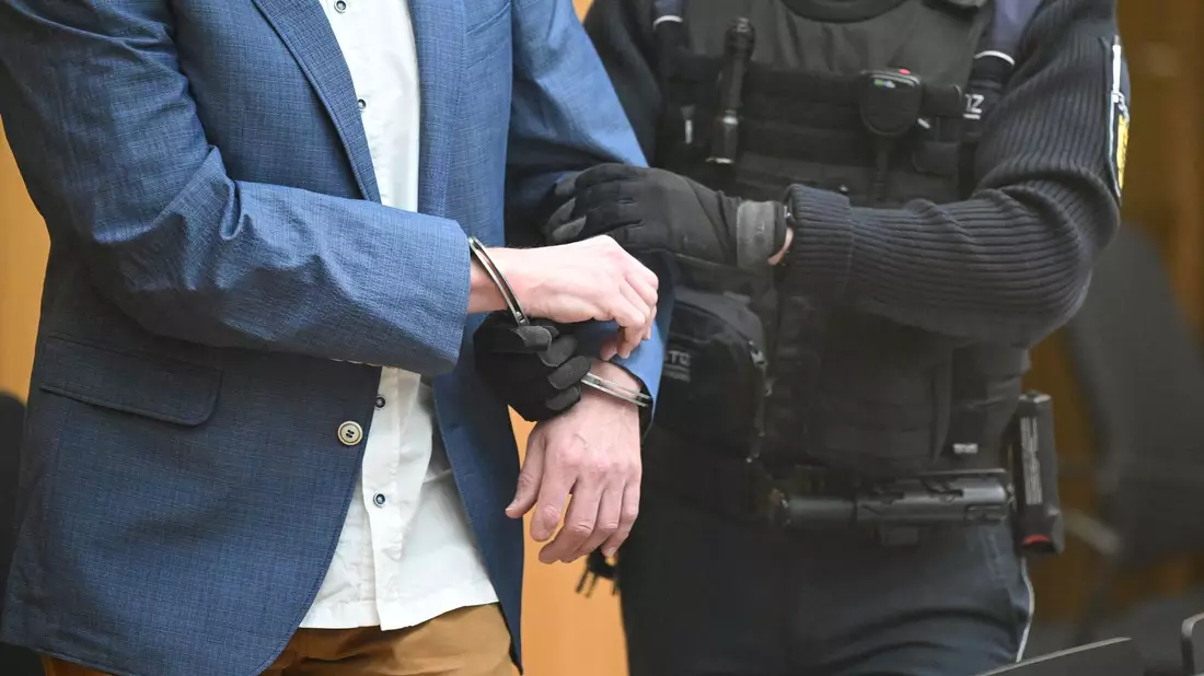 Ein Angeklagter bei Prozessbeginn in den Gerichtssaal geführt. - Bild: Bernd Weißbrod/dpa