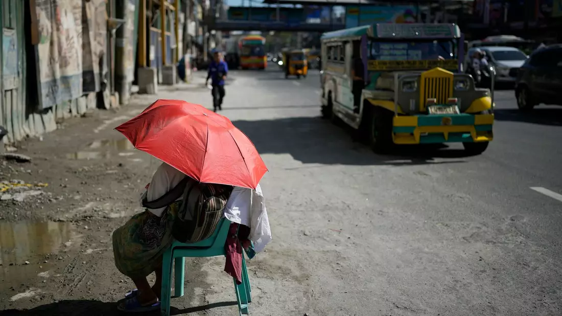 Eine Straßenverkäuferin schützt sich in Manila mit einem Regenschirm vor der Sonne. - Bild: Aaron Favila/AP/dpa