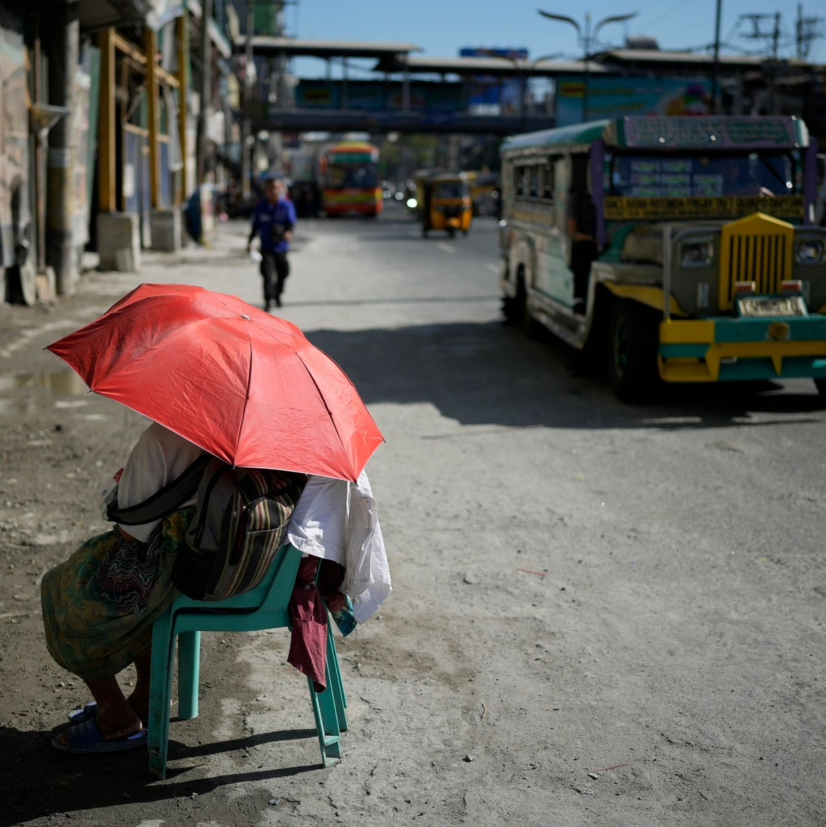 Eine Straßenverkäuferin schützt sich in Manila mit einem Regenschirm vor der Sonne. - Foto: Aaron Favila/AP/dpa
