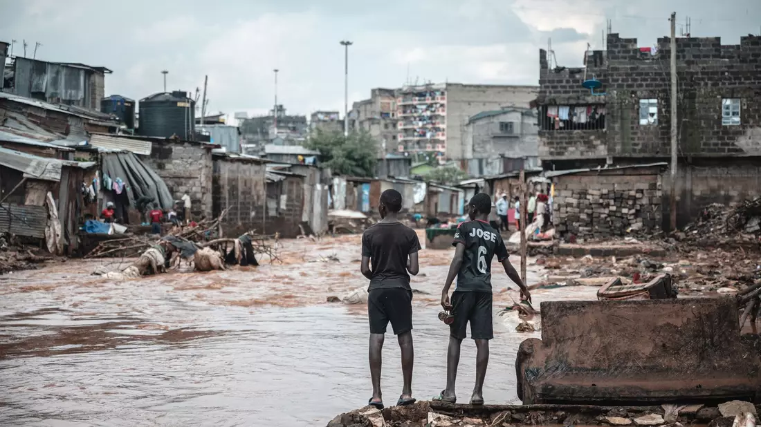 Menschen stehen am Ufer eines überfluteten Flusses in den Mathare-Slums in Nairobi. - Bild: Wang Guansen/XinHua/dpa