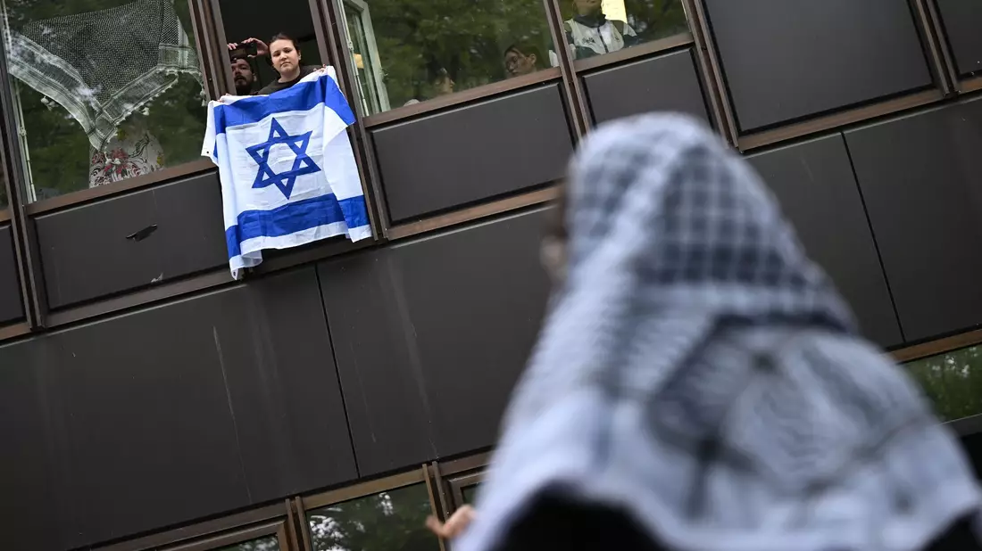Eine Frau hält eine Israelflagge aus dem Fenster: Die propalästinensische Demonstration auf dem Theaterhof der Freien Universität Berlin wird von Polizisten beobachtet. - Bild: Sebastian Christoph Gollnow/dpa